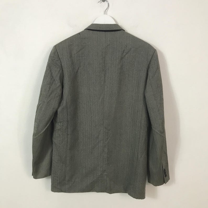 May include: A grey blazer with a subtle vertical stripe pattern, hanging on a white hanger. The back of the jacket is visible, showing the collar and buttoned cuffs. The blazer is made of a textured fabric.