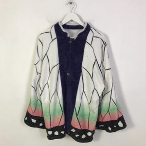 May include: A long-sleeve jacket featuring a white base with a black butterfly wing pattern. The garment has a solid dark purple centre panel with two gold-tone snap buttons. The hem and sleeve cuffs transition into a gradient of green and pink.