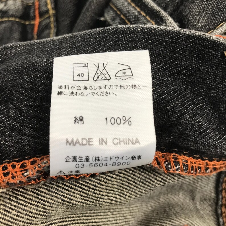 May include: Close-up of a denim garment label. The label displays washing instructions, including a 40-degree wash symbol. The text on the label reads "100% Cotton" and "Made in China."