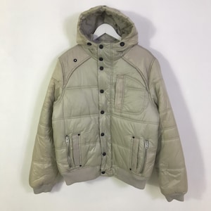 Könnte beinhalten: Beige Steppjacke mit Kapuze, schwarzen Knöpfen und zwei Reißverschlusstaschen. Die Jacke hat einen gerippten Saum und Bündchen. Die Jacke hängt an einem weißen Kleiderbügel.