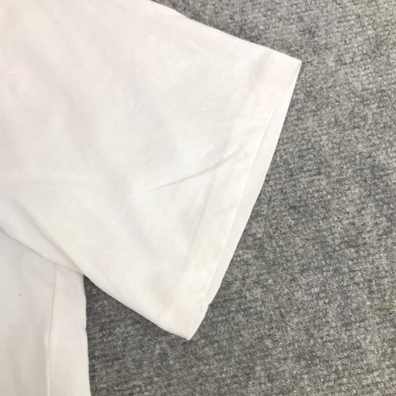 May include: Close-up of the white cotton fabric of a t-shirt sleeve. The fabric is smooth and wrinkle-free.