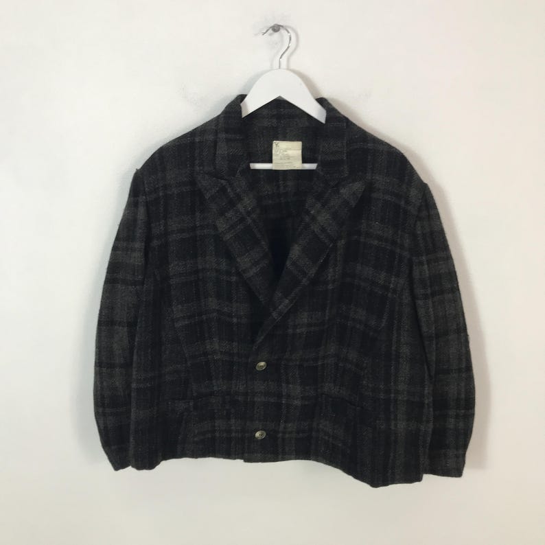 May include: A dark grey and black checked blazer with two buttons, hanging on a white hanger. The jacket has a classic collar and a tailored fit. The fabric appears to be a wool blend.