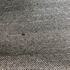 May include: Close-up of a black and white herringbone fabric. The fabric features a repeating chevron pattern, with alternating black and white stripes creating a textured appearance. The weave is tight, and the pattern is consistent across the surface.