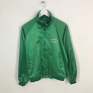 Puede incluir: Una chaqueta de satén verde con cierre de cremallera y un logotipo bordado en blanco que dice "FUJICOLOR" en la espalda. La chaqueta tiene un cuello, puños y dobladillo de canalé.