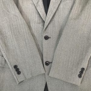 May include: A light grey blazer with a subtle textured pattern. The jacket features three buttons on the front and three buttons on each sleeve cuff. The blazer has a classic notched lapel and a tailored fit.