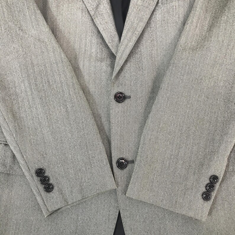 May include: A light grey blazer with a subtle textured pattern. The jacket features three buttons on the front and three buttons on each sleeve cuff. The blazer has a classic notched lapel and a tailored fit.