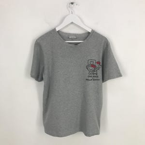 Pu&ograve; includere: T-shirt grigio a maniche corte con scollo a V. La maglietta presenta una piccola grafica sul davanti con la scritta "ONE PIECE HELLO KITTY". La grafica &egrave; un personaggio dei cartoni animati con cappello e fiocco.
