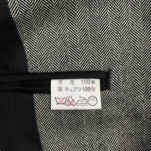 May include: Close-up of a black and white herringbone pattern fabric. A white tag with Japanese text and care symbols is visible. The fabric appears to be a wool blend.