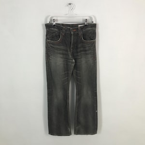 May include: Dark gray denim jeans with a faded wash, hanging on a white hanger. The jeans have a classic five-pocket design with orange stitching and a slight bootcut leg opening. The jeans are a size 34.