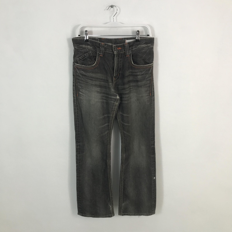 May include: Dark gray denim jeans with a faded wash, hanging on a white hanger. The jeans have a classic five-pocket design with orange stitching and a slight bootcut leg opening. The jeans are a size 34.