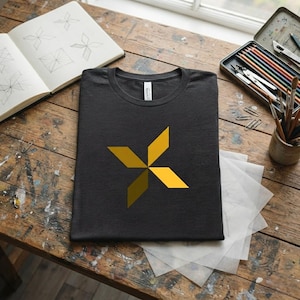 Könnte beinhalten: Ein anthrazitfarbenes T-Shirt mit einer geometrischen, vierzackigen Sternengrafik auf der Brust. Der Stern besteht aus vier rautenförmigen Segmenten in verschiedenen Gelb- und Goldtönen, die ein symmetrisches, windradartiges Design bilden.