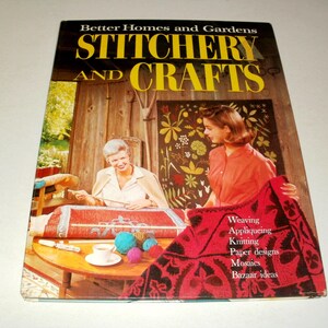 May include: A vintage book cover for "Better Homes and Gardens Stitchery and Crafts." The cover features two women, one working on a rug and the other holding a red textile. The book's title is in yellow, with a list of crafts below.