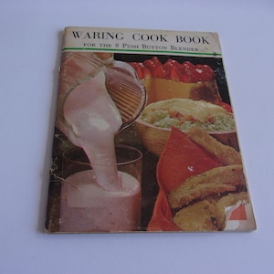 May include: Vintage "Waring Cook Book" for the 8 Push Button Blender. The cover features a colorful illustration of food, including a strawberry dessert, a bowl of salad, and fried food. A pink liquid is being poured into a glass.