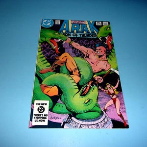 May include: A comic book titled Arak Son of Thunder featuring a muscular character with a mohawk fighting a large green snake. A blonde character in a red outfit stands nearby. The cover includes the DC logo and the text The New DC There's No Stopping Us Now.