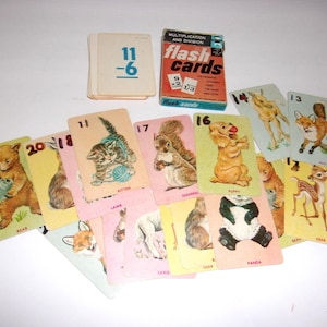 May include: A collection of vintage educational flash cards featuring multiplication and division problems alongside illustrated animal cards. The box is labeled "Multiplication and Division flash cards" and includes various cards depicting a bear, kitten, squirrel, puppy, fox, panda, and deer.