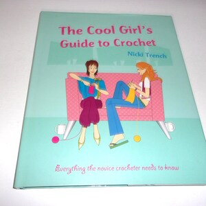 May include: A book titled "The Cool Girl's Guide to Crochet" by Nicki Trench. The cover features illustrations of two women crocheting on a pink couch, set against a light teal background. The text "Everything the novice crocheter needs to know" is also visible.