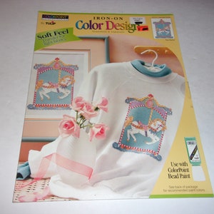 May include: An iron-on Color Design transfer sheet by Tulip, featuring a carousel horse design. The image shows the design on a sweatshirt and framed art, with a vase of pink roses. The text reads "Soft Feel".