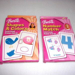 May include: Two Barbie learning game card sets in rectangular boxes. The left box is orange and pink, titled Shapes & Colors, featuring a blue bird and pink circle card. The right box is pink, titled Number Match, showing ladybugs and the number 4.