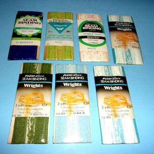 May include: An assortment of vintage seam binding packages in various colors, including blue, green, and white. The packages feature the "Wright's" brand and text indicating the material and length of the binding, which is 3 yards.