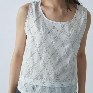 Può includere: Top senza maniche bianco con un motivo geometrico grigio scuro. Il top ha uno scollo tondo e un design a strati. Il tessuto sembra leggero e adatto al clima caldo. Lo stile è casual e minimalista.