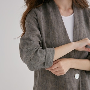 May include: A brown plaid blazer with a single white button. The blazer has long sleeves that are rolled up at the elbow. The fabric has a subtle checkered pattern.