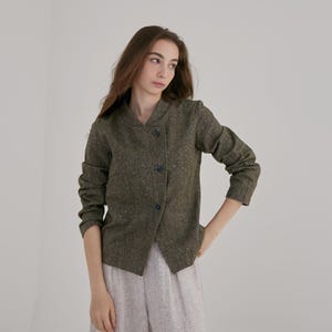 Peut inclure: Une veste en tweed vert avec un col et une fermeture à bouton unique. La veste a un design légèrement asymétrique et est faite d'un tissu doux et texturé.