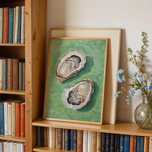 Op de afbeelding: Een ingelijst schilderij van twee oesters op een groene achtergrond. De oesters zijn open en de binnenkant van de schelpen is zichtbaar. Het schilderij hangt aan een muur met een boekenkast aan beide kanten.
