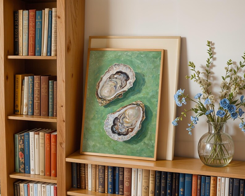 Op de afbeelding: Een ingelijst schilderij van twee oesters op een groene achtergrond. De oesters zijn open en de binnenkant van de schelpen is zichtbaar. Het schilderij hangt aan een muur met een boekenkast aan beide kanten.