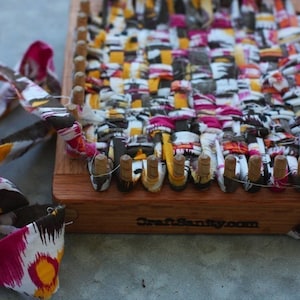 May include: A close-up of a wooden loom with colorful fabric strips woven into a pattern. The loom has a wooden frame and wooden pegs. The fabric strips are a mix of pink, yellow, white, and brown. The loom is labeled "Craft Sanity.com".