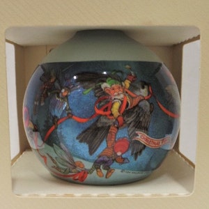 May include: A round glass Christmas ornament with a blue background and a scene of elves flying through the air with a banner that reads "Christmas Time". The ornament is in a white box with the words "Flights of Fantasy" and "Keepsake Ornament" printed on it.
