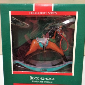May include: A vintage 1989 rocking horse ornament in a green box. The ornament is made of wood and painted brown, red, and blue. The horse has a saddle and a bridle. The box has the words "Collector's Series" and "Rocking Horse Handcrafted Ornament Dated 1989" printed on it.