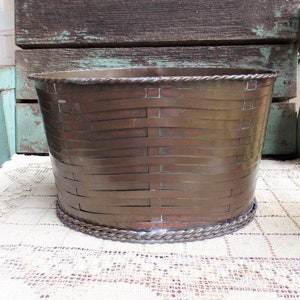 May include: A woven copper planter with a rope trim. The planter is sitting on a white crocheted doily.