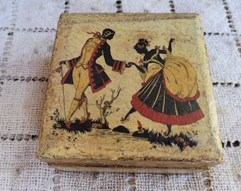 May include: A small wooden box featuring a painted scene of a man and woman dancing. The man is dressed in a black and red suit, while the woman wears a yellow and black dress. The box is adorned with a gold trim.