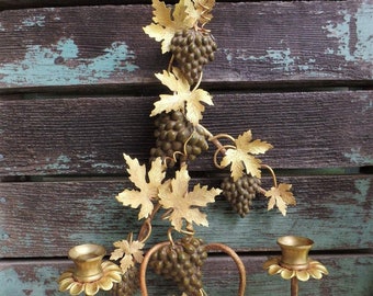 May include: Gold metal wall sconce with a grapevine design and two candle holders. The sconce is decorated with gold leaves and grapes.