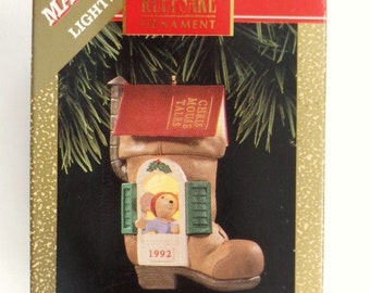 May include: A Hallmark Keepsake ornament featuring a brown boot with a red roof and a window with a small mouse inside. The ornament is part of the Chris Mouse Tales collector's series and is dated 1992.