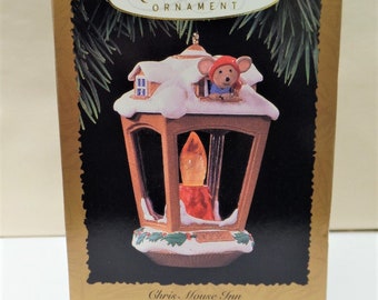 May include: A gold Keepsake Ornament box with a light-up Christmas House Inn ornament featuring a mouse peeking out of the window. The box reads "Keepsake Ornament" and "Magic Collector's Series".