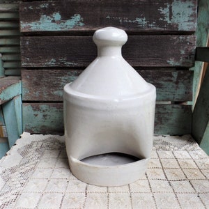 May include: A white ceramic chicken feeder with a rounded top and a single opening on the front. The feeder is sitting on a white crocheted doily.