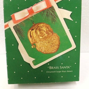 Puede incluir: Una caja verde con una cinta blanca y un adorno de Santa Claus de latón dorado. La caja tiene lunares blancos y el texto "BRASS SANTA" y "Adorno más grande que el que se muestra".