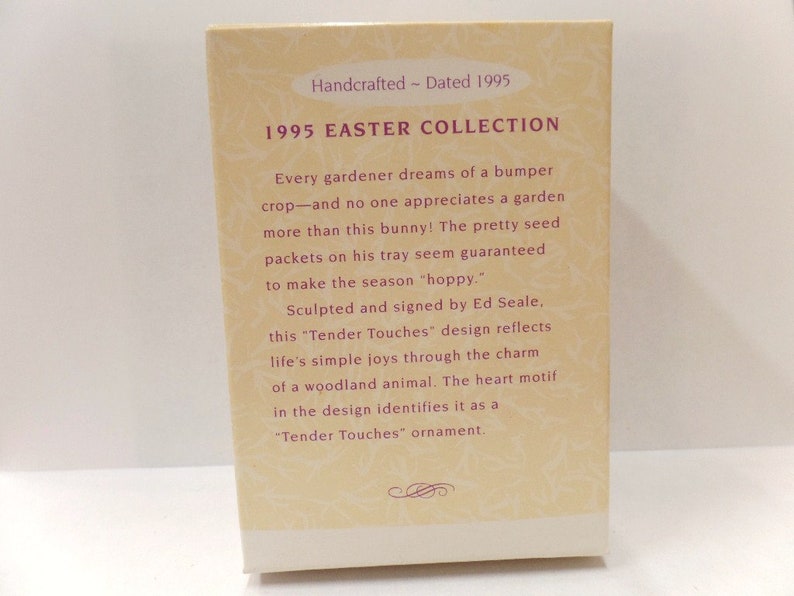 以下が含まれることがあります： 「1995 EASTER COLLECTION」と書かれたクリーム色の箱。テキストはウサギと種子のパックについて説明しています。箱には「Handcrafted - Dated 1995」と書かれており、Ed Sealeによって署名されています。