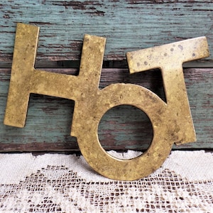 Puede incluir: Letras de latón que deletrean la palabra "HOT" en un estilo vintage. Las letras están ligeramente desgastadas y tienen un color dorado cálido.