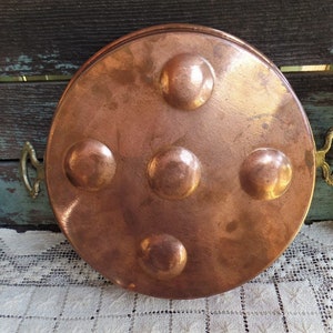 May include: A vintage copper serving tray with five raised circular indentations and two brass handles. The tray is round and has a hammered finish.