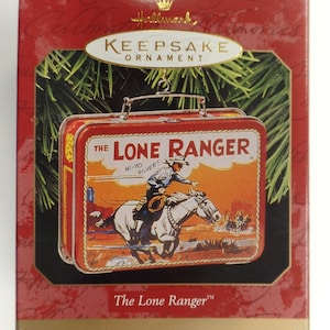 May include: A red and yellow metal lunchbox ornament with a picture of The Lone Ranger riding his horse Silver. The lunchbox has the text "The Lone Ranger" and "Hi-Yo Silver!" on it. Hallmark Keepsake Ornament.