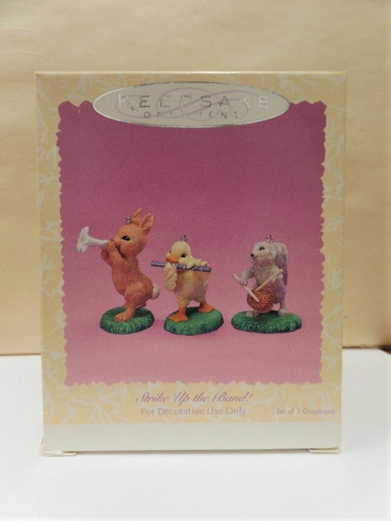 Puede incluir: Un conjunto de tres adornos de colecci&oacute;n que representan un conejo tocando la trompeta, un pato tocando la flauta y una ardilla tocando el tambor. Los adornos forman parte de la colecci&oacute;n "Strike Up the Band!" y son solo para uso decorativo.