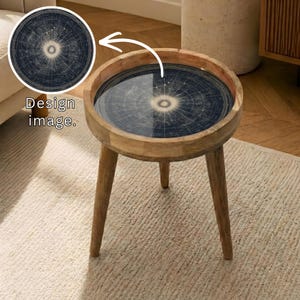 May include: A round wooden side table with a dark blue and cream celestial map design on the tabletop. The table has three angled legs and a raised rim. The text "Design image" is in the upper left corner.