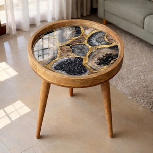 May include: A round side table with a natural wood frame and three angled legs. The tabletop features a geode design with black, brown, gold, and grey tones. The table is approximately 51 cm in diameter.