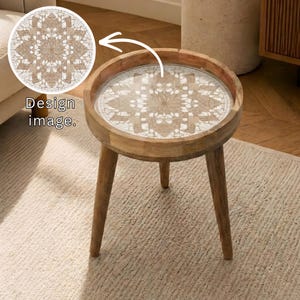Könnte beinhalten: Ein runder Beistelltisch aus Holz mit einer dekorativen, gemusterten Oberseite. Der Tisch hat drei abgewinkelte Beine und einen erhöhten Rand. Die Oberseite hat ein beige-weißes Design. Der Text "Design image" ist im Bild.
