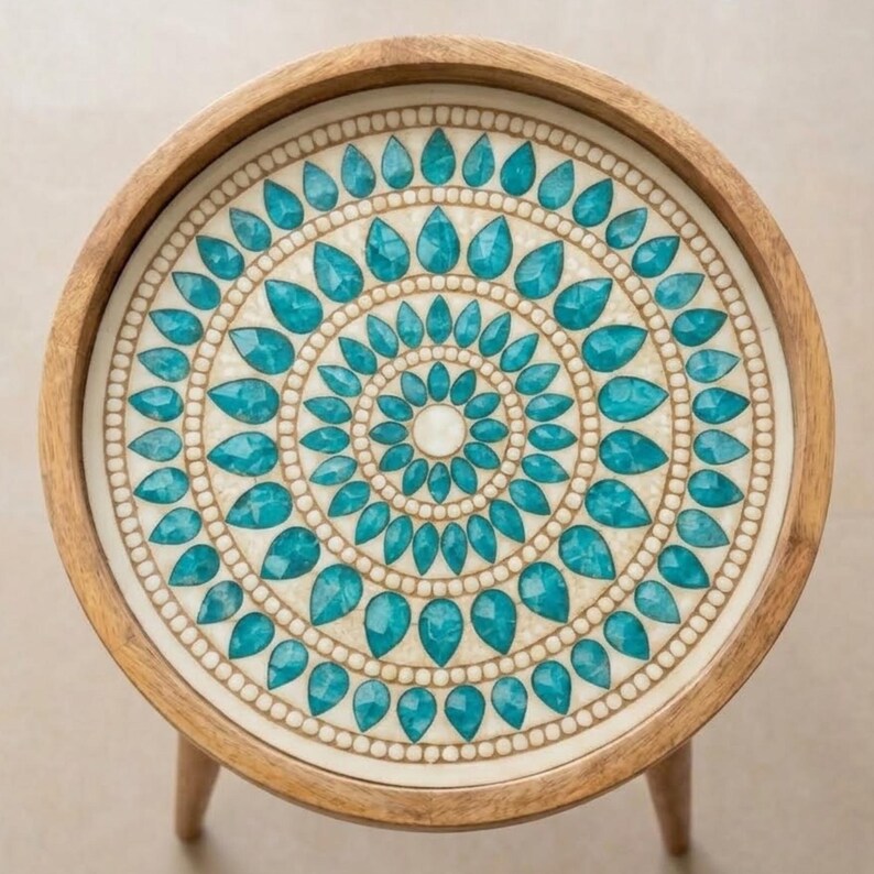 May include: A round wooden side table with a light brown frame and a circular tabletop featuring a decorative inlay. The inlay consists of concentric rings of teal, teardrop-shaped stones set against a cream-coloured background with small beads.