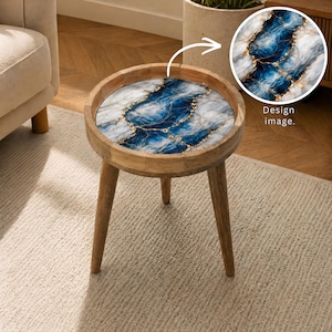 May include: A round wooden side table with three tapered legs and a circular tabletop featuring a blue, white, and gold marbled resin design. An inset circular graphic shows the same blue, white, and gold marbled pattern with the text Design image.