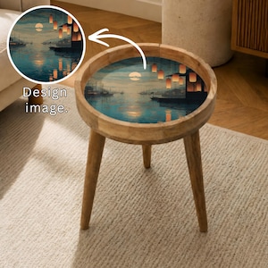 May include: A round wooden side table with a scenic design on the tabletop. The design features a moonlit harbor scene with boats and hanging lanterns. The table has three angled legs and a natural wood finish.