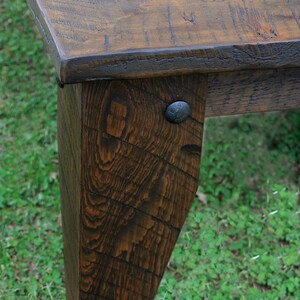 May include: A close-up of a wooden table leg with a dark brown stain. The leg is made of reclaimed wood and has a rustic look. A metal nail is visible on the leg.
